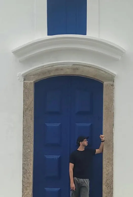 Thiago Queiroz em frente a uma porta azul colonial